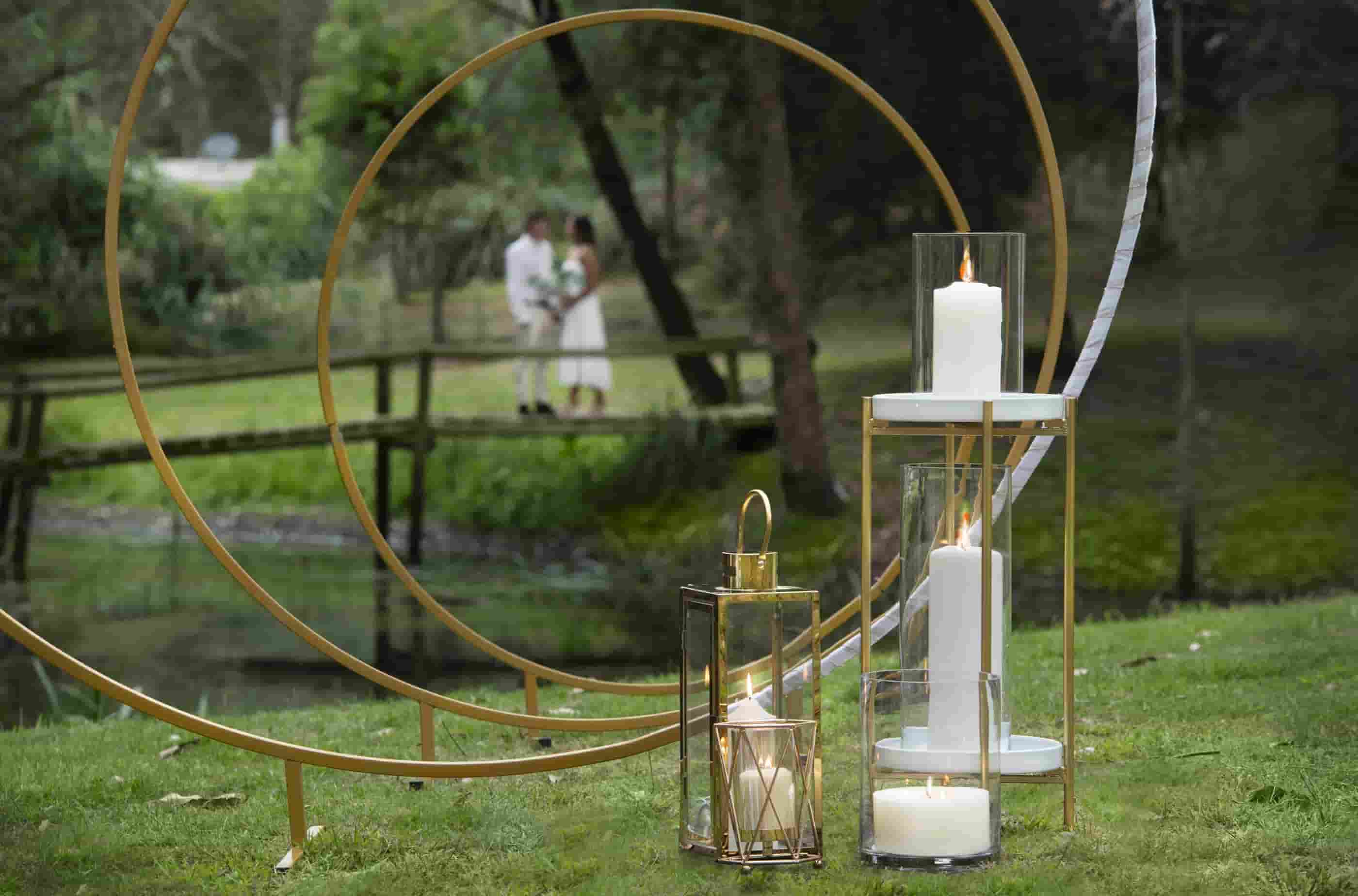 Three gold rings with candles with a bride and groom in the background